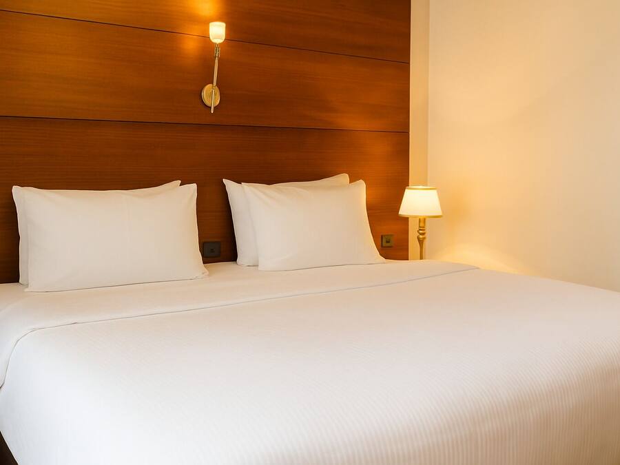 Una cama bien hecha con sábanas blancas, un cabecero de madera y una lámpara de noche.