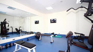 Un gimnasio con equipo de ejercicio, una banca y un espejo grande.