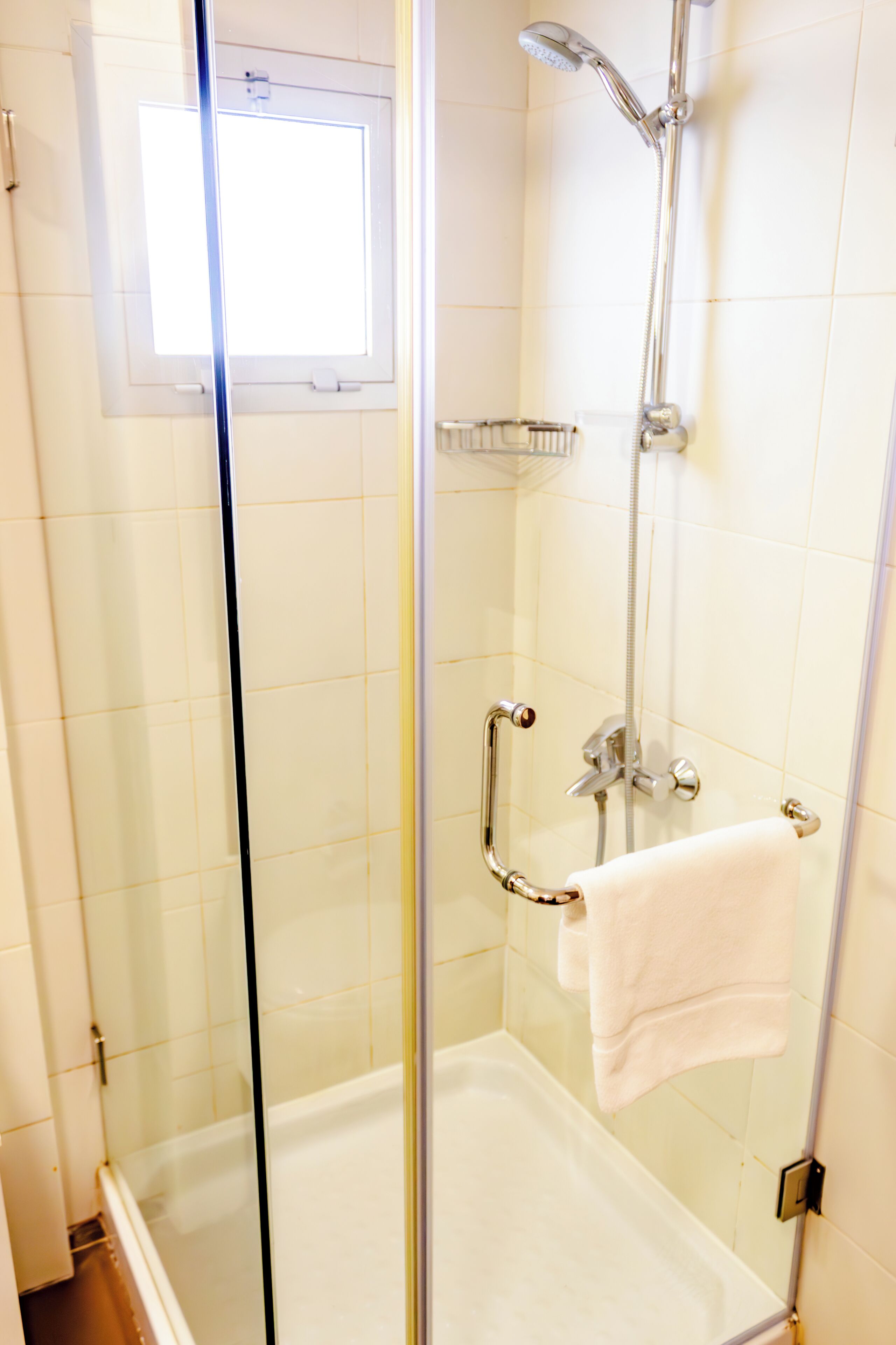 A glass-enclosed shower with a handheld showerhead, a handheld shower control, and a towel rack with a towel.