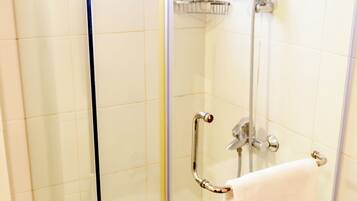 A glass-enclosed shower with a handheld showerhead, a handheld shower control, and a towel rack with a towel.