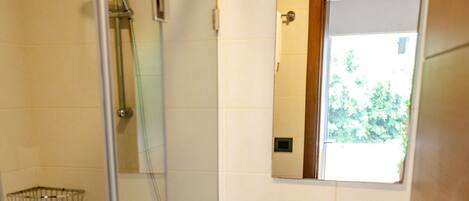 Un baño con ducha de vidrio, lavamanos blanco y espejo encima.