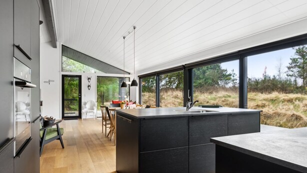 A modern kitchen with a large island, wooden flooring, and a view of the outdoors.