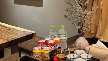 A hotel room with a wooden side table holding snacks, drinks, and a vase with dried flowers.