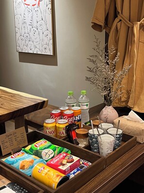 A hotel room with a wooden side table holding snacks, drinks, and a vase with dried flowers. - Brilliant Nature Suites & Spa (Hanoi)