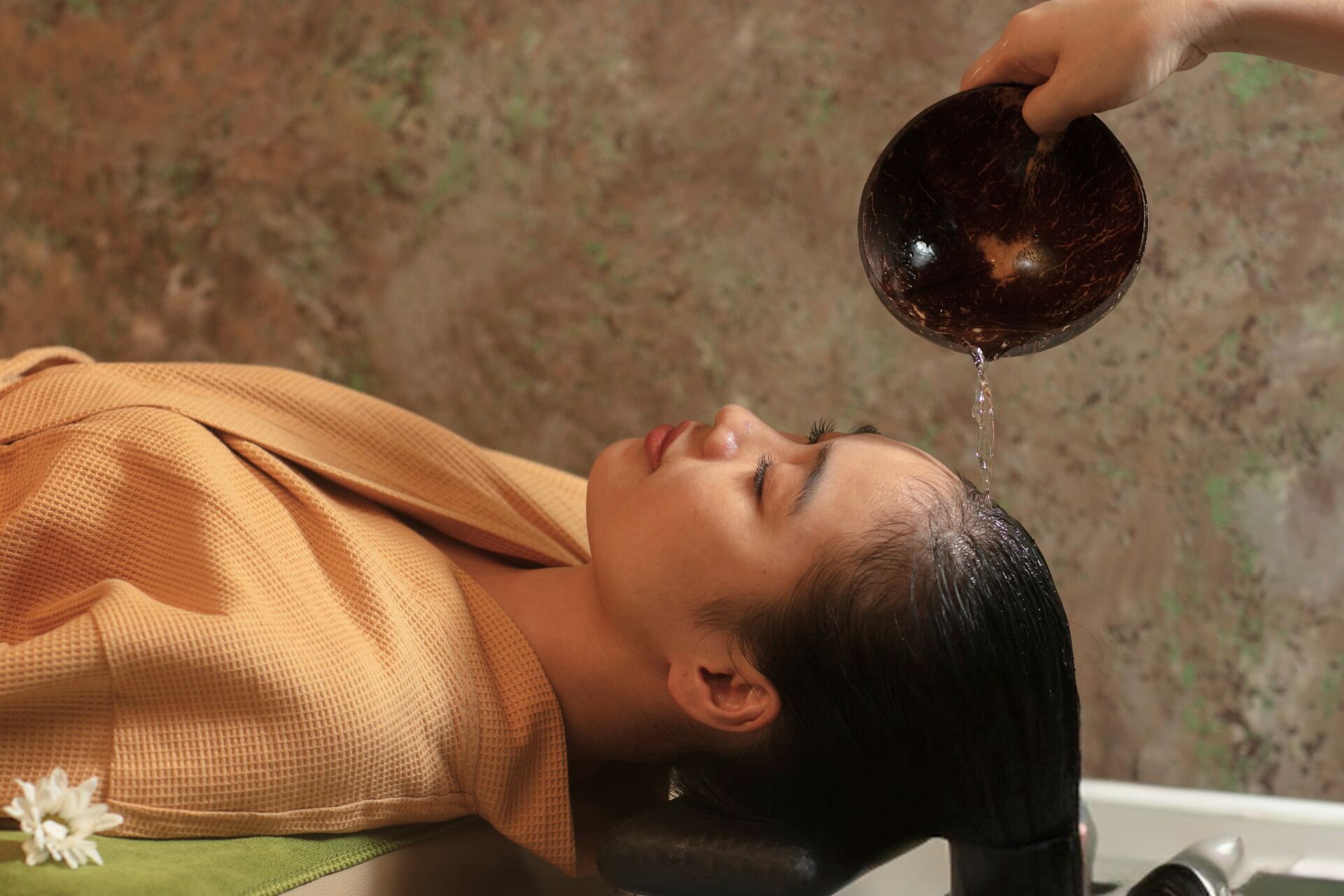 A person lying down with a bowl being poured over their head.