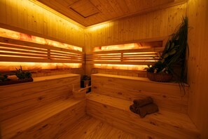 A sauna with wooden benches and slatted backrests, a basket with plants, and a towel on the floor. - Brilliant Nature Suites & Spa (Hanoi)