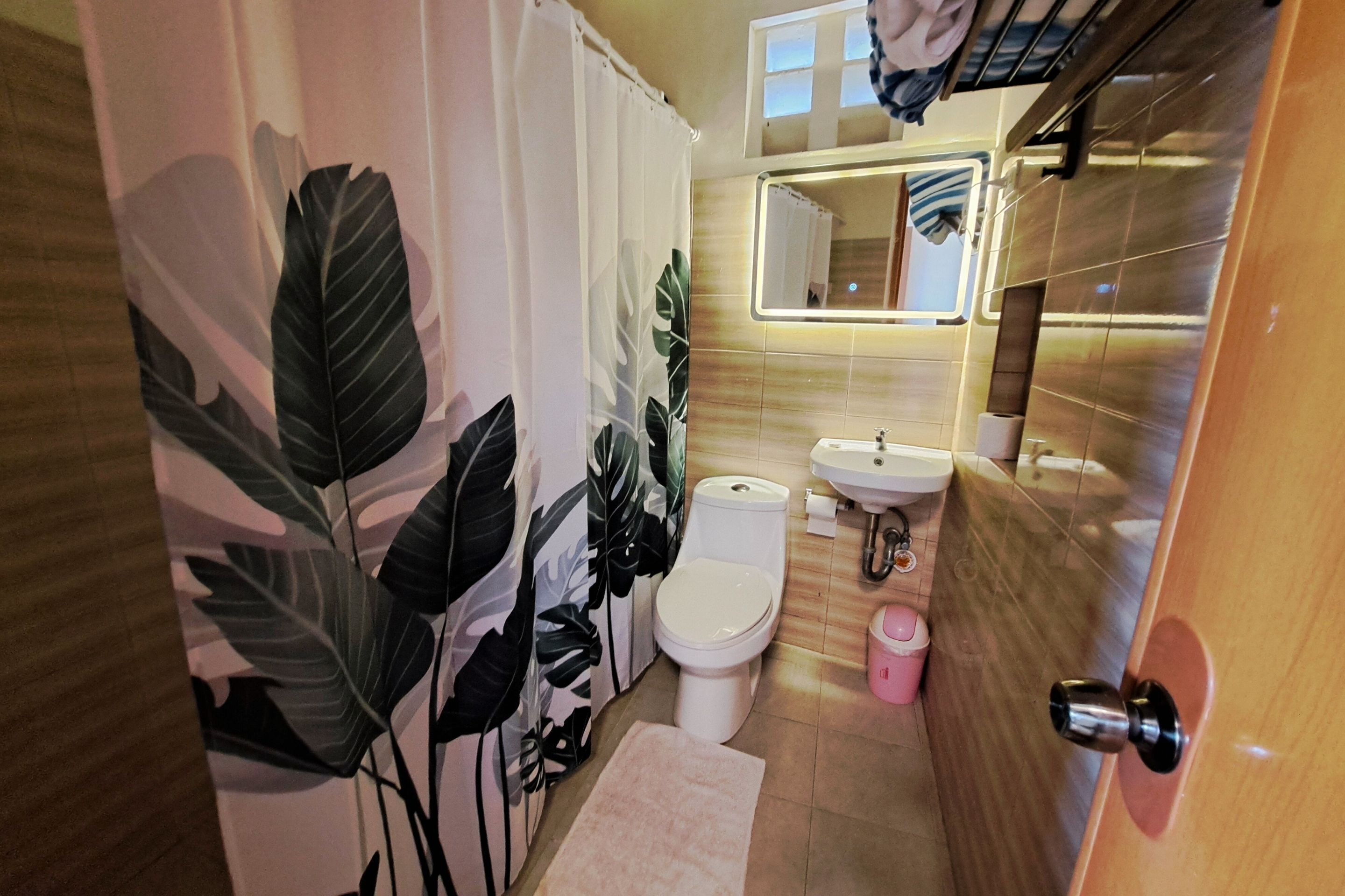 Et badeværelse med toilet, vask og bruseforhæng med bladmotiv.