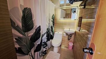 Et badeværelse med toilet, vask og bruseforhæng med bladmotiv.