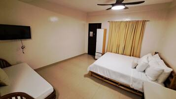A bedroom with a bed, a desk, a chair, a TV mounted on the wall, and a ceiling fan.