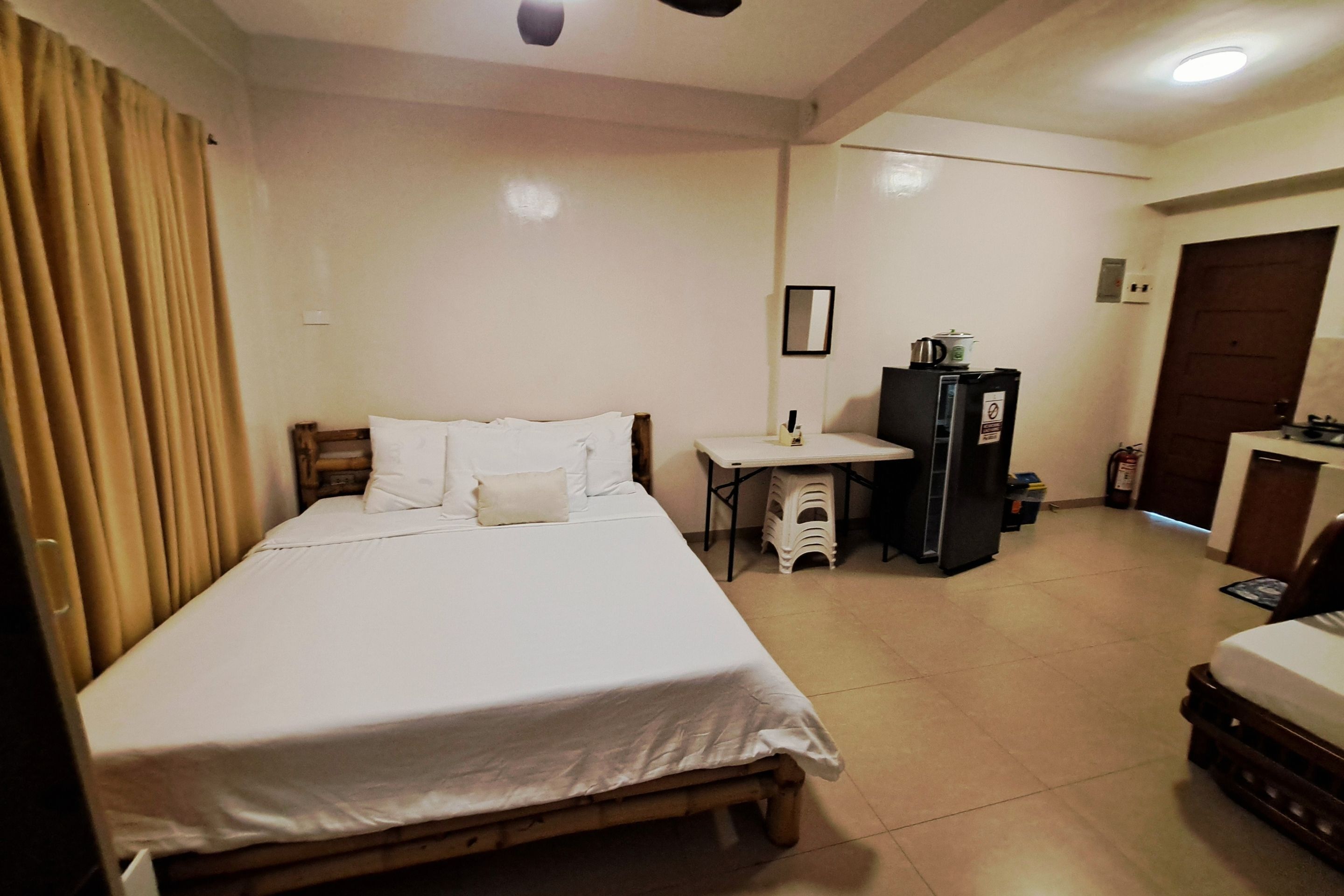 A hotel room with a bed, a small table, a refrigerator, and a door.