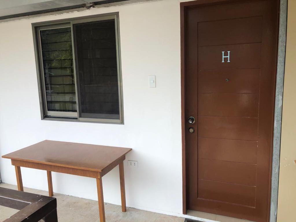 A room with a wooden table, a window with blinds, and a brown door marked with an 'H'.