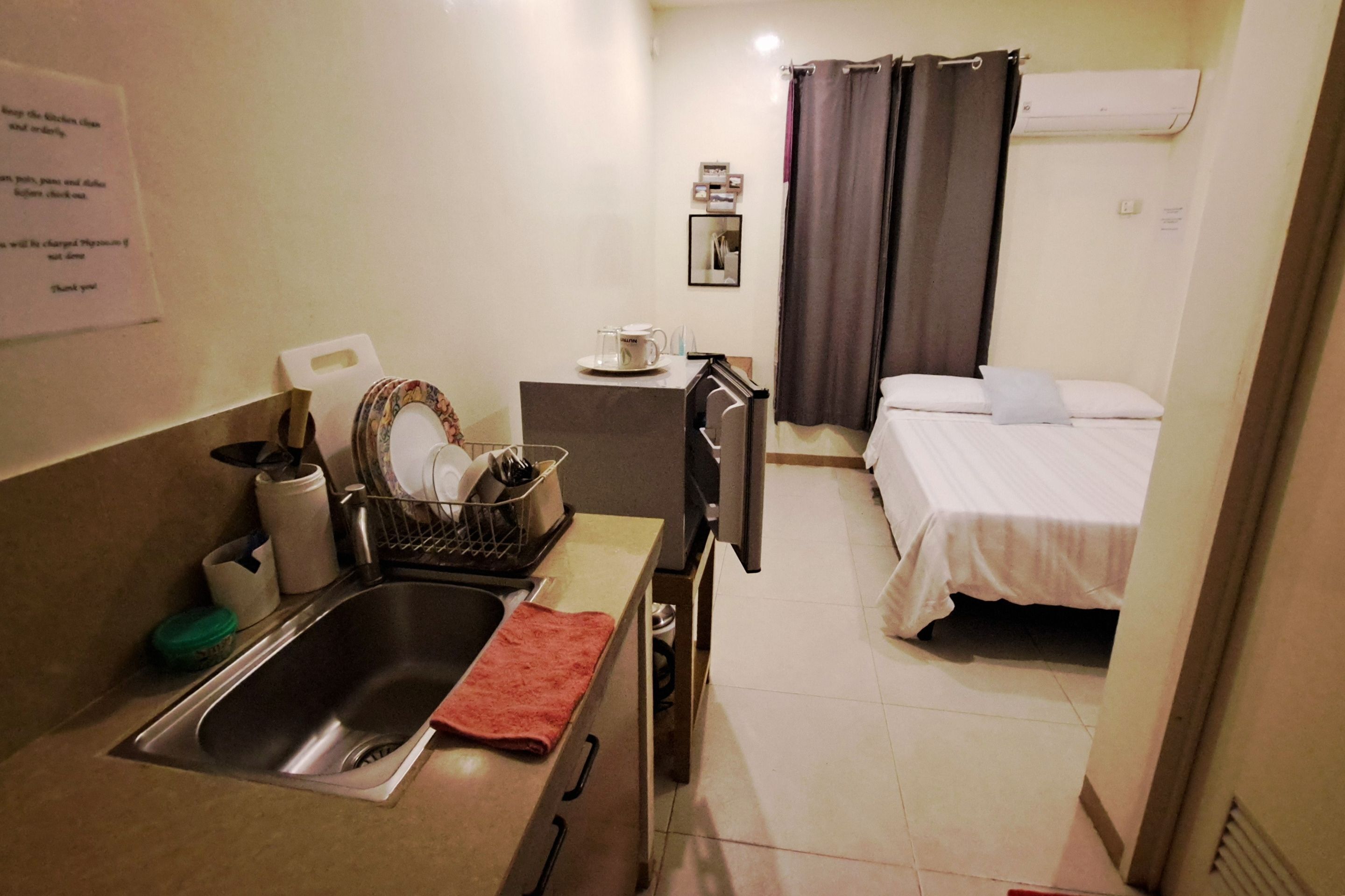 A compact hotel room with a kitchenette, a bed, a small bathroom, and a shower area.