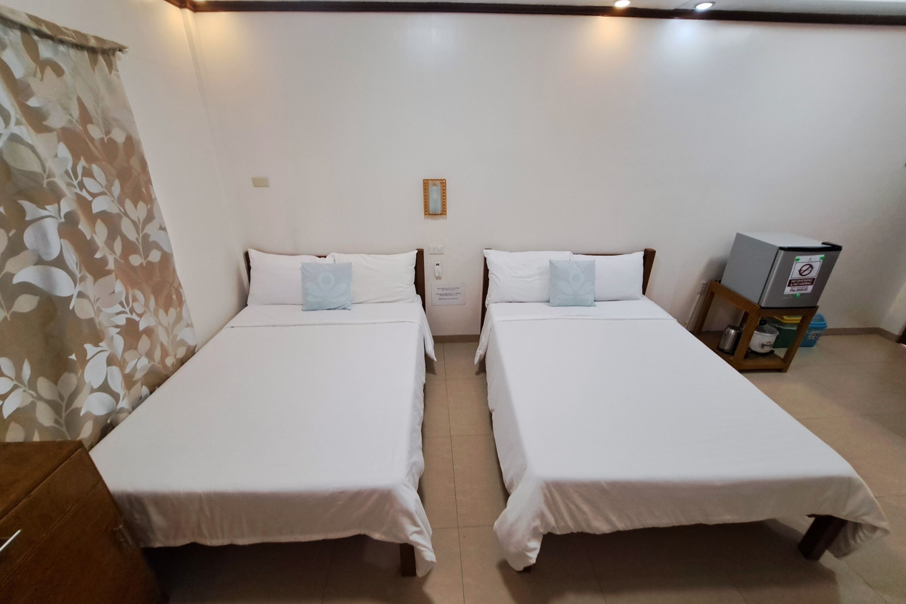 Une chambre d’hôtel avec deux lits simples, une table de chevet en bois, une petite table et un téléviseur fixé au mur.