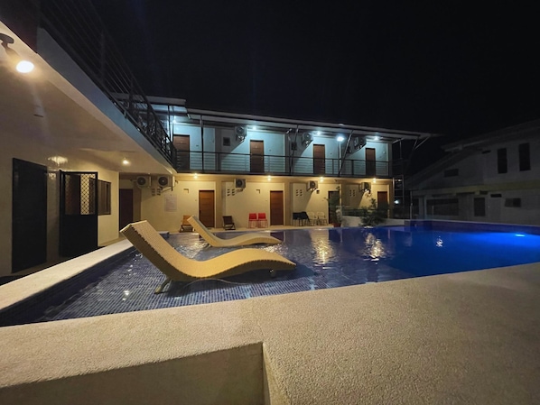 A swimming pool with lounge chairs, a building with multiple floors, and outdoor seating.