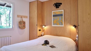 A bedroom with a large bed, wooden wardrobe, a window with a view of trees, a wall-mounted lamp, and a framed picture. - Villa Marina de Talaris sur le lac de Lacanau (Lacanau)