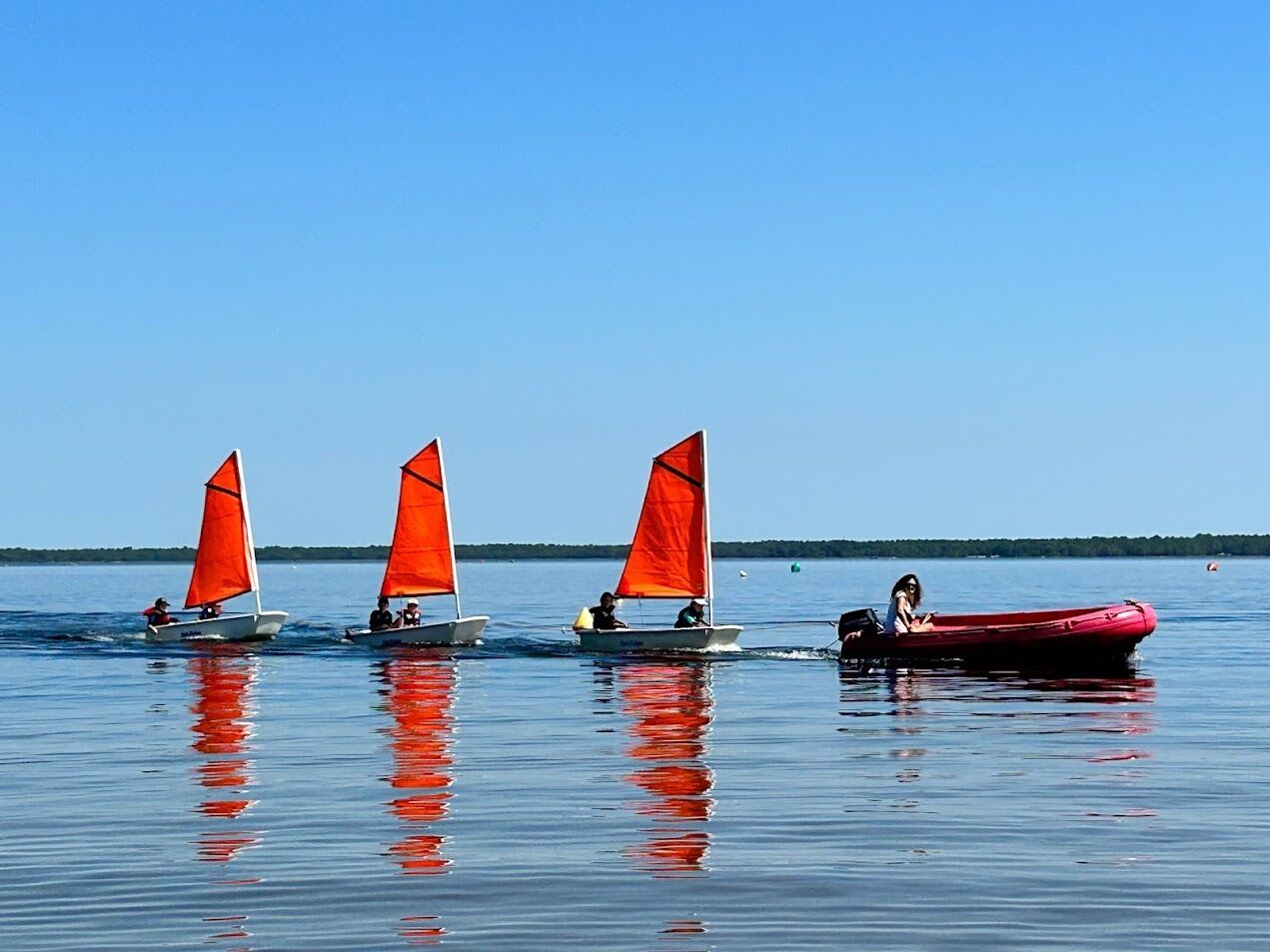 Three sailboats with red sails on calm water.