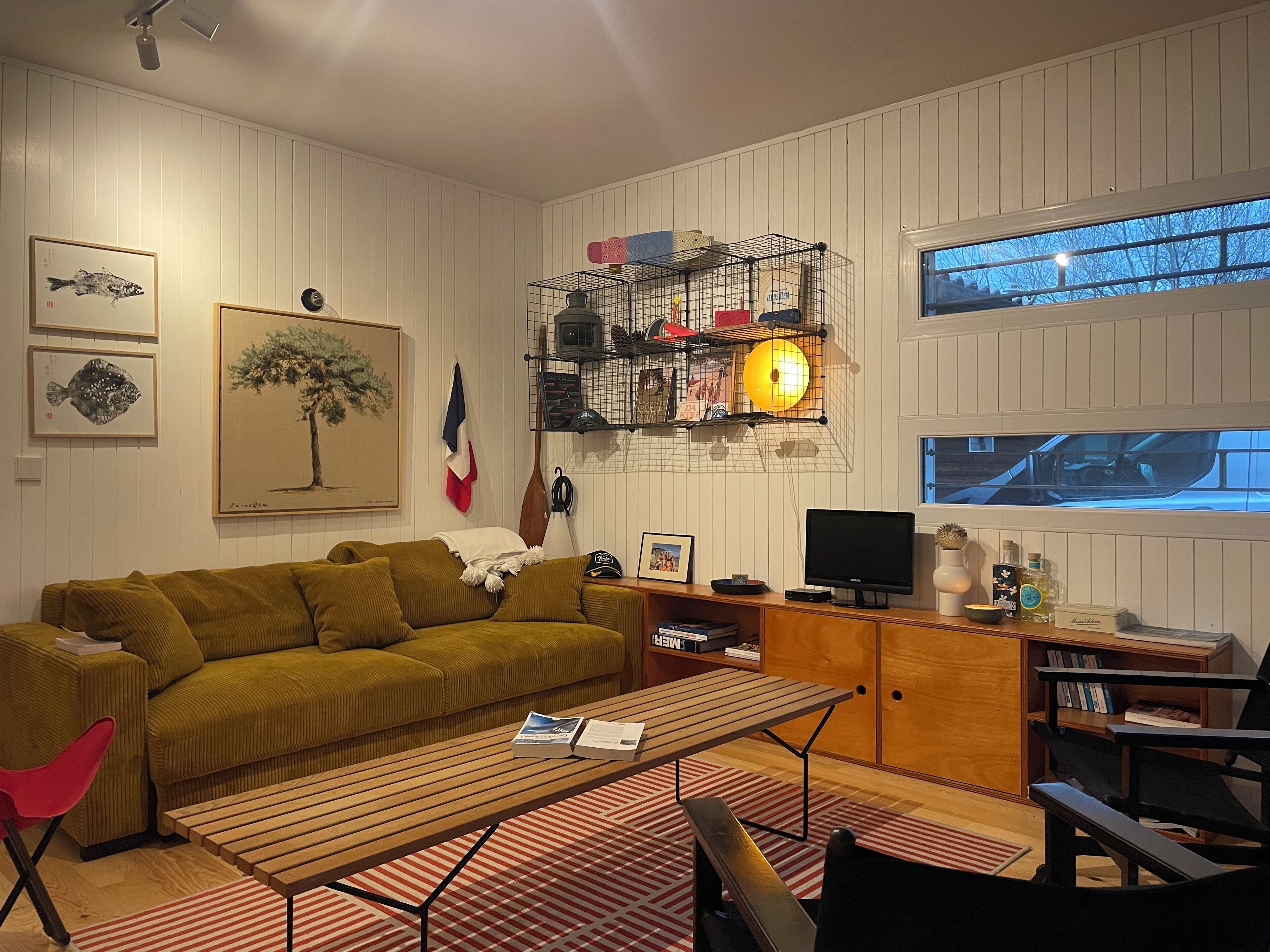 A living room with a sofa, a coffee table, a TV, a bookshelf, and a window with a view of a car.