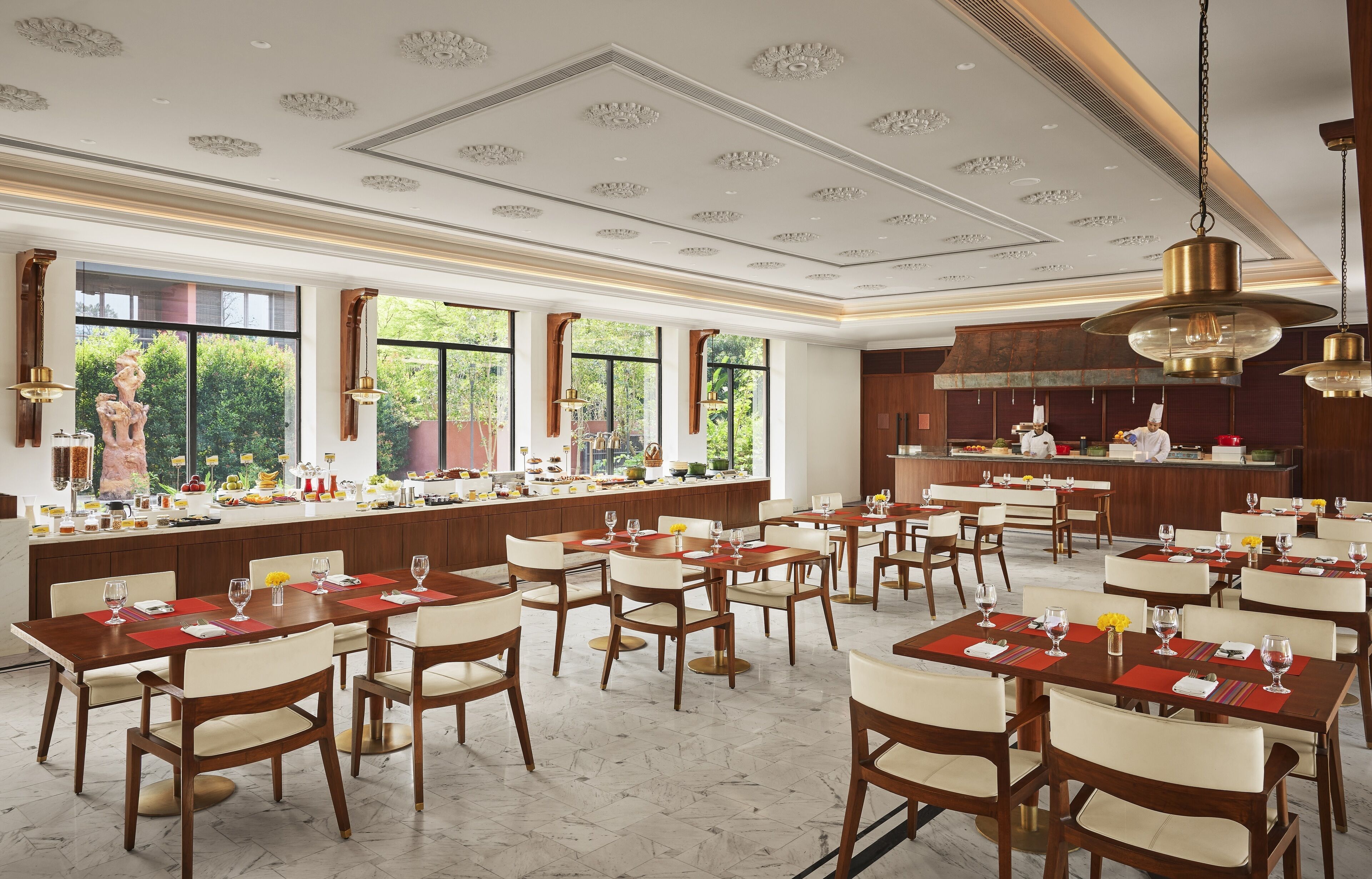 Un grand espace dédié à la salle à manger, avec plusieurs tables et chaises, une cuisine à l’arrière-plan et de grandes fenêtres qui laissent entrer la lumière naturelle.