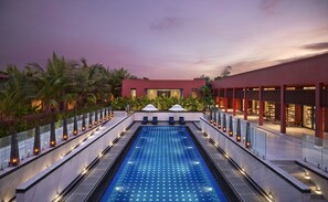 Un área de piscina con diseño moderno, rodeada de palmeras y un edificio con amplios ventanales.