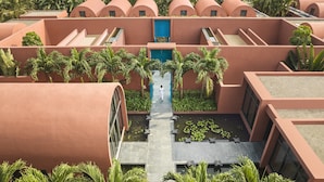 Un hotel moderno con edificios color terracota, un patio central con fuentes de agua y abundante vegetación que lo rodea.