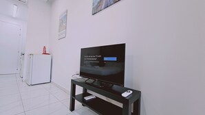 A modern hotel room with a flat-screen TV on a black stand, a small table with a remote control, and a white door in the background. - STAY Terra Cota Studio (Limassol)