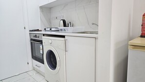 A compact kitchen with a built-in washer and dryer, a small countertop, and a sink. - STAY Terra Cota Studio (Limassol)