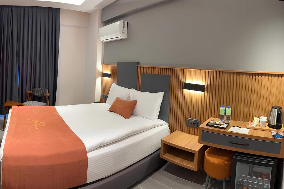 Habitación de hotel con cama, mesita de noche, escritorio, silla y espejo.