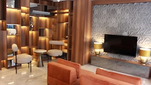 A modern living room with a flat-screen TV, orange sofas, and a wooden shelving unit with built-in lighting. - Roi Hotel Izmir (Izmir)