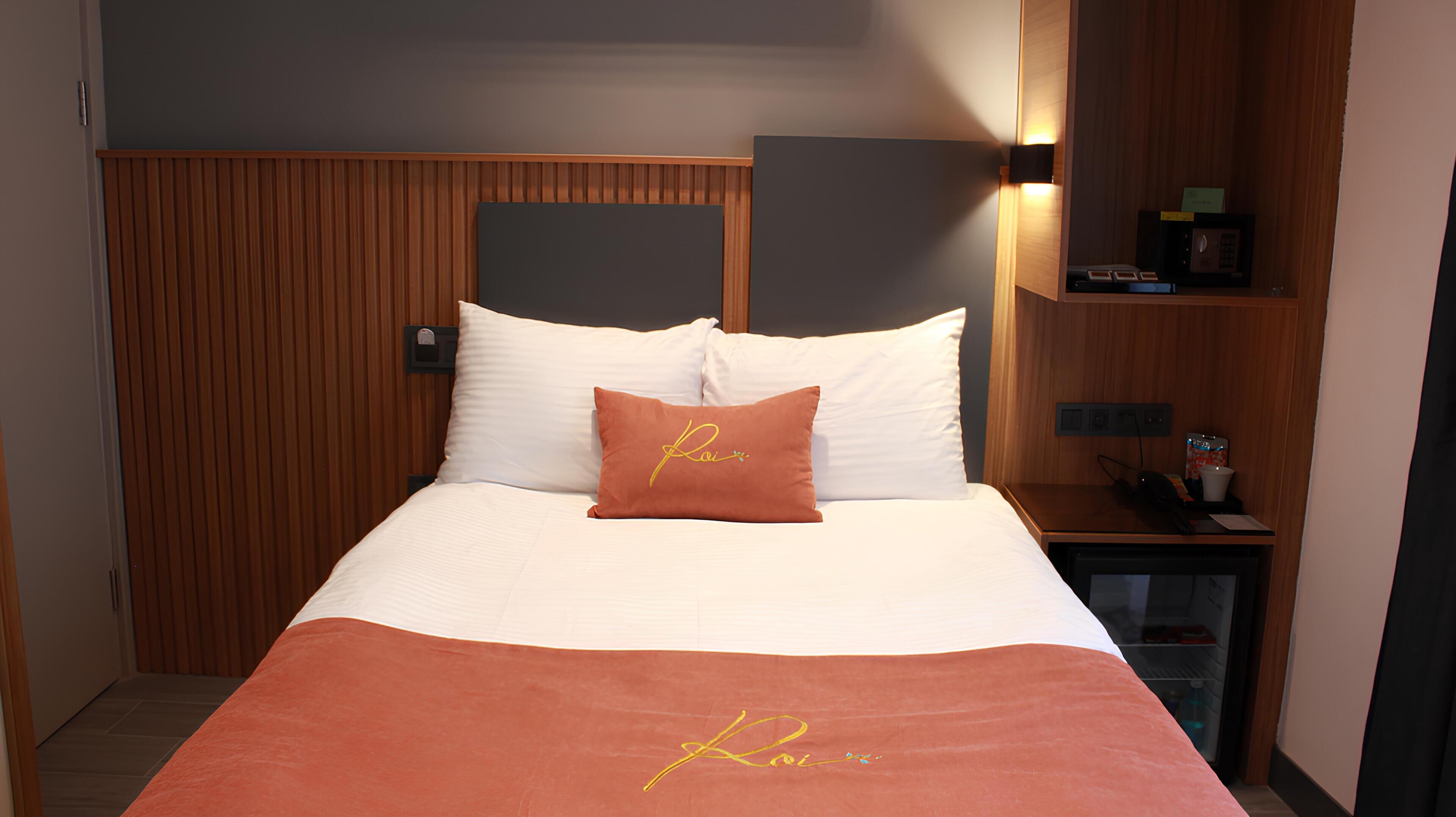 A hotel room with a bed, a nightstand, a wall-mounted shelf, and a wooden panel wall.