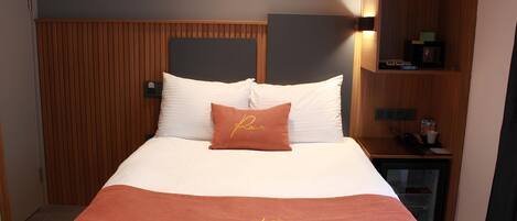 Habitación de hotel con cama, mesita de noche, estante en la pared y pared de paneles de madera.