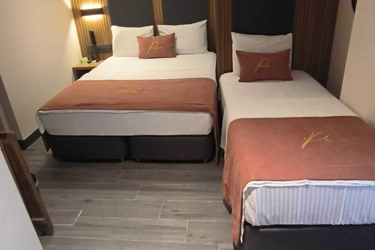 Habitación de hotel con dos camas, una mesita de noche, una lámpara y aire acondicionado instalado en la pared.