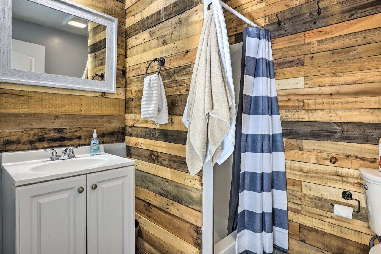 Une salle de bain avec un mur en bois, un lavabo blanc, un miroir, un rideau de douche à rayures et un porte-serviettes.