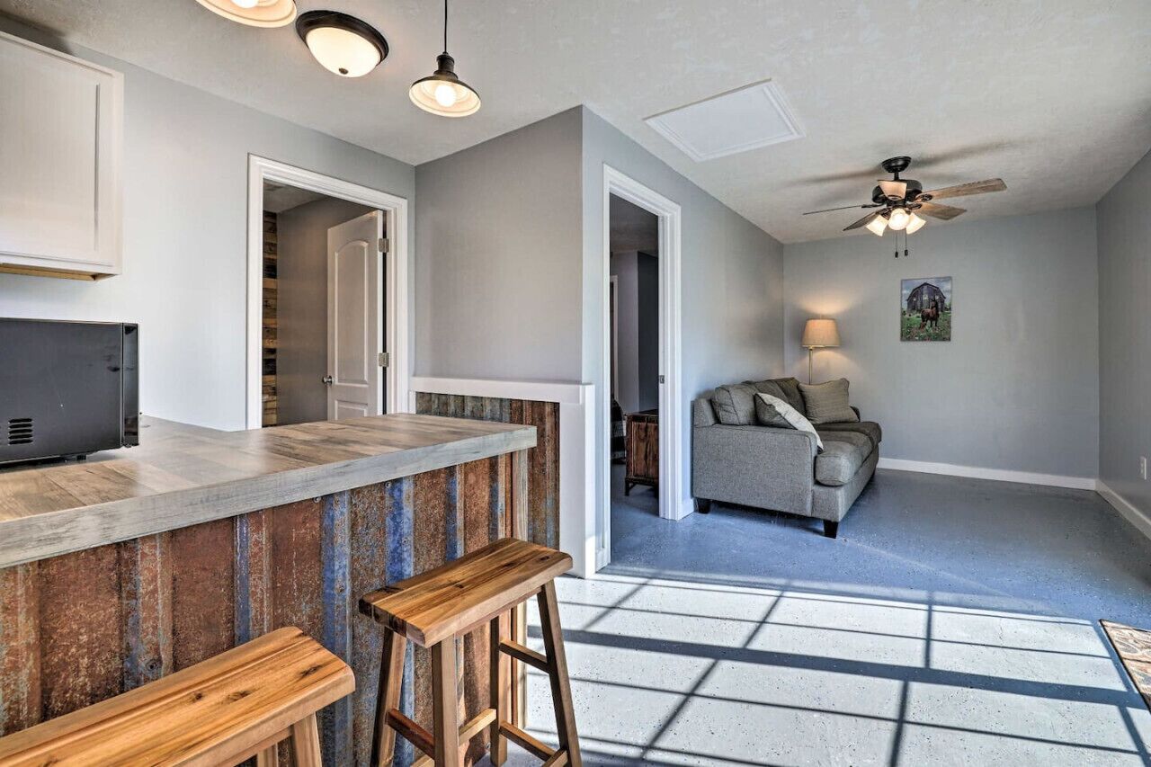 Une cuisine avec un coin bar, un ventilateur de plafond et une vue sur un salon comprenant un canapé et une lampe.