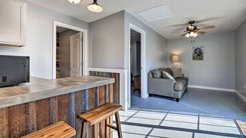 Une cuisine avec un coin bar, un ventilateur de plafond et une vue sur un salon comprenant un canapé et une lampe.