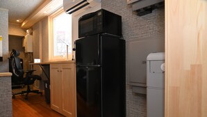 Una cocina compacta con un refrigerador negro, un microondas encima y un pequeño electrodoméstico blanco a la derecha.