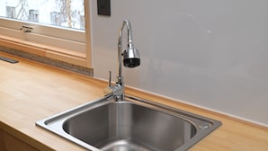 Un lavamanos de acero inoxidable con un grifo moderno, encimera de madera y una ventana encima.