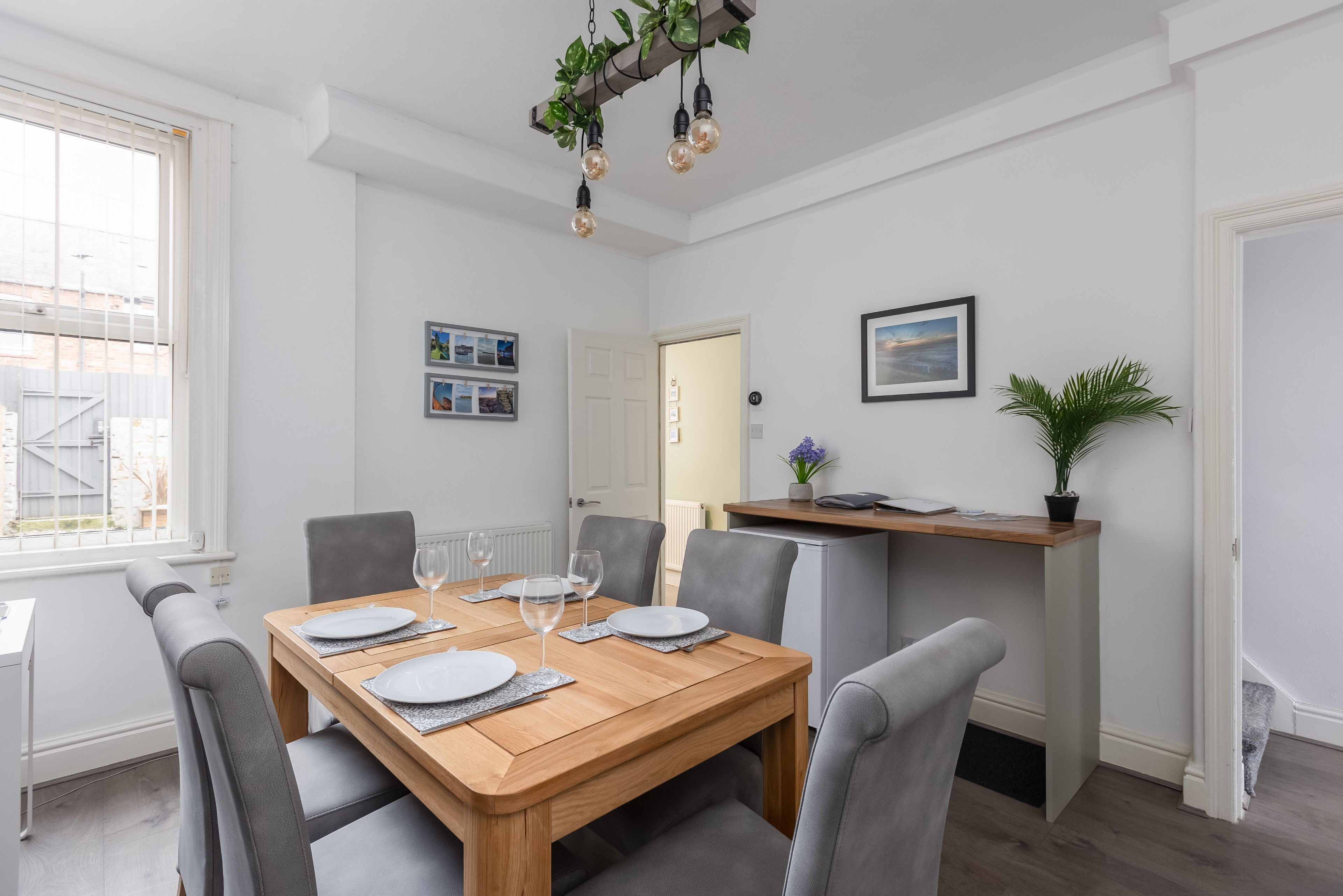A dining area with a wooden table set for four, grey upholstered chairs, and a pendant light fixture.