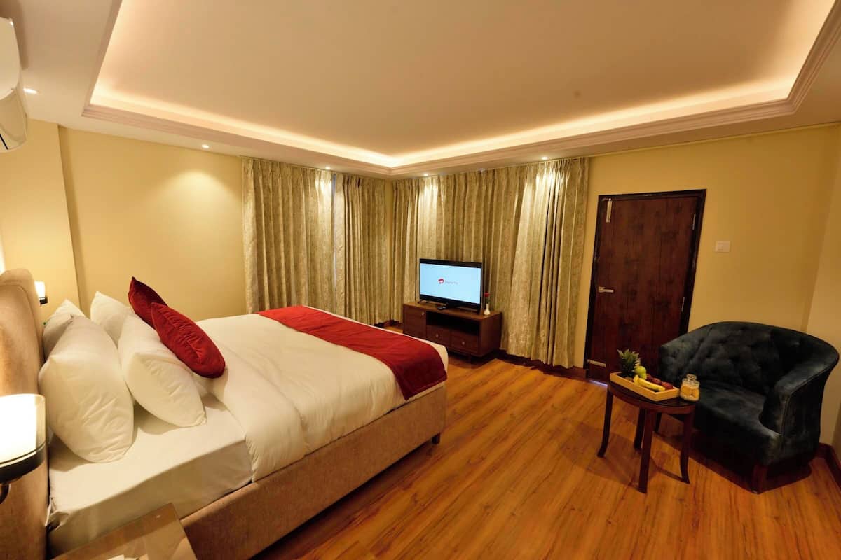 A hotel room with a bed, a television, a chair, and a small table with fruit.
