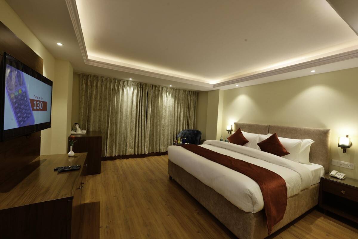 A hotel room with a large bed, a desk with a television, a telephone, and a nightstand.