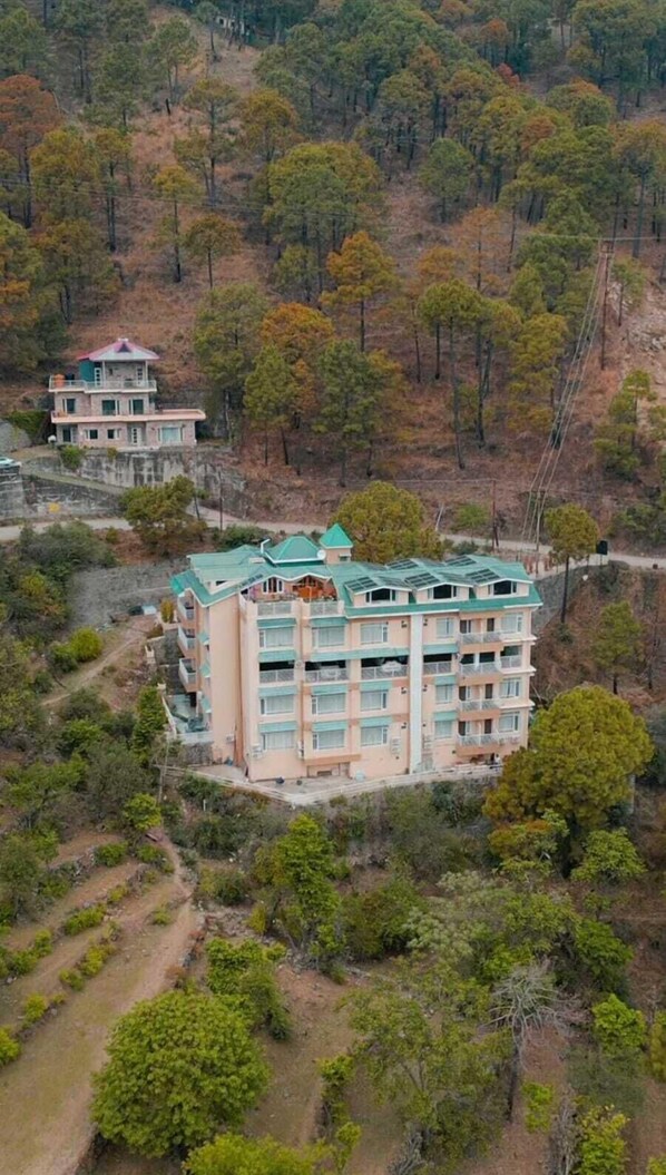 A multi-story hotel with balconies, surrounded by forested hills.