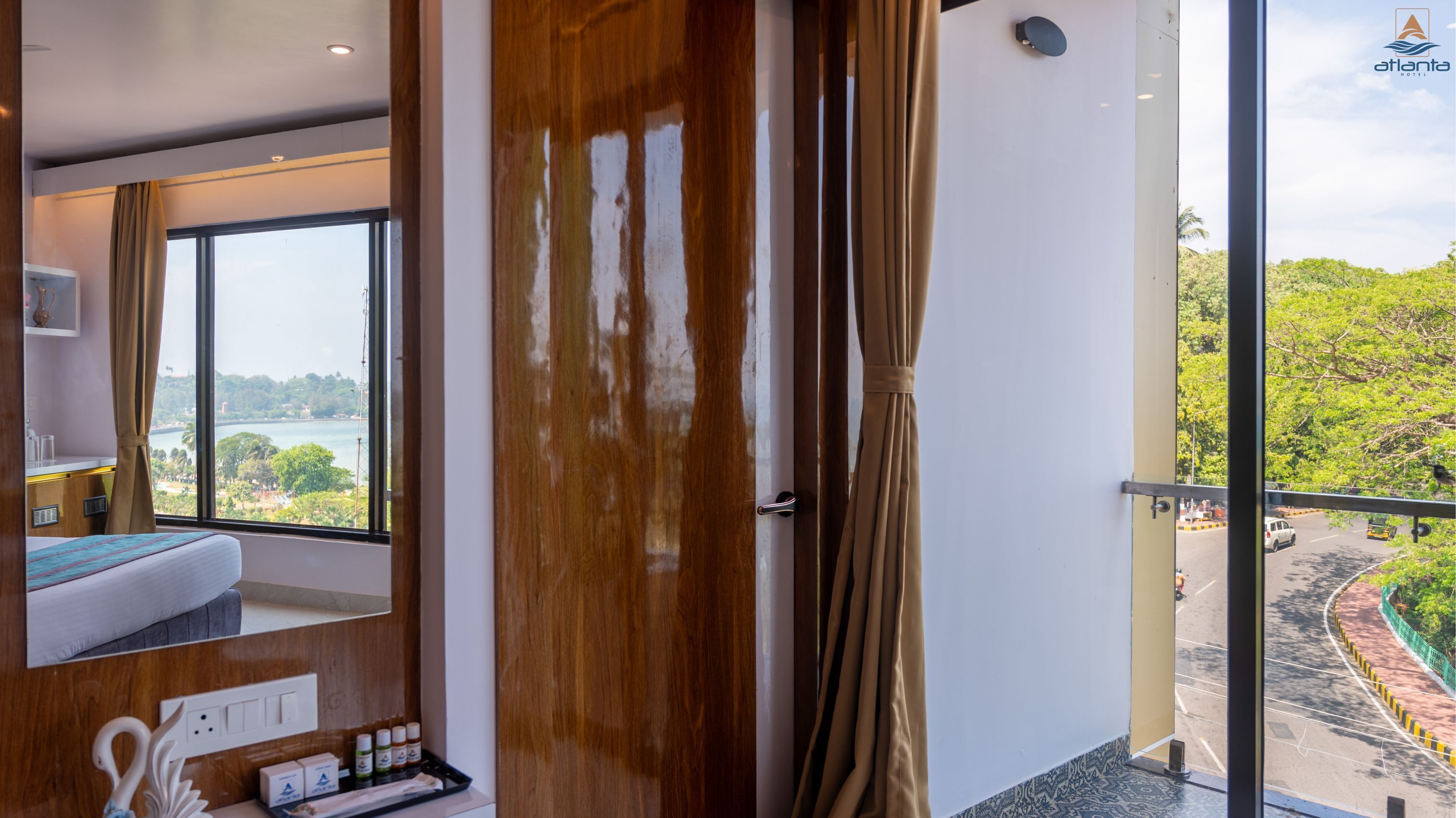 A hotel room with a large window, a bed, a mirror, and a view of a road and greenery.