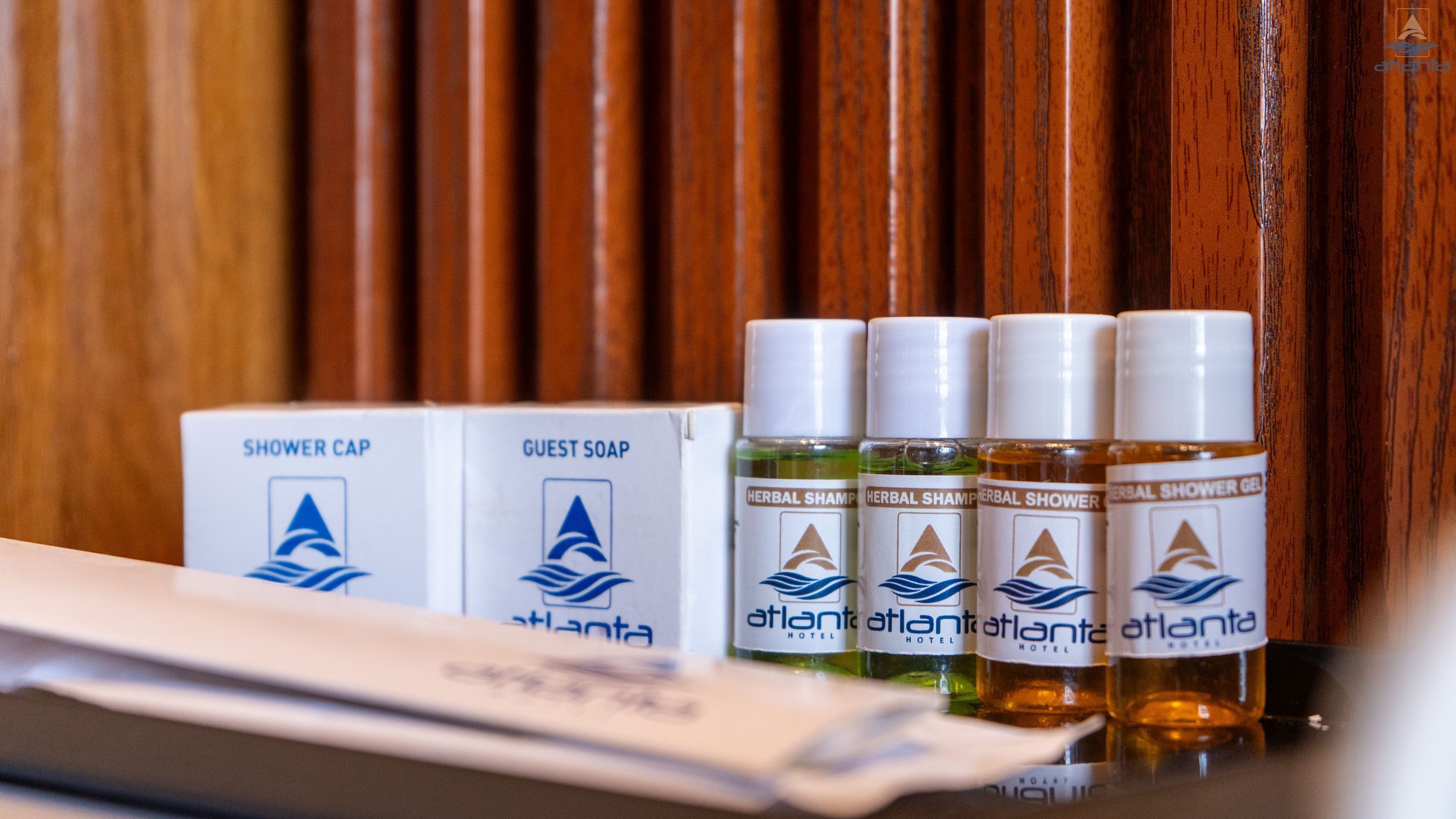 A hotel bathroom with wooden paneling, a shower cap, guest soap, and bottles of herbal shampoo and shower gel.