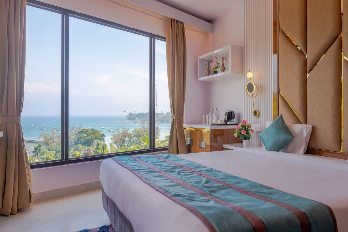 Hotelkamer met een groot bed, een bureau met koffiezetapparaat, een plank met decoratieve items en uitzicht op de oceaan.