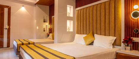 A hotel room with two beds, a wooden headboard, a bedside table with a mirror, and a small vase with flowers.