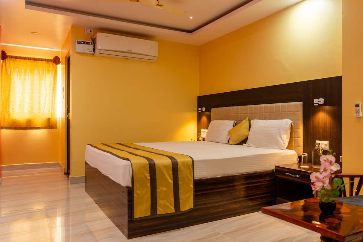Een hotelkamer met een groot bed, een nachtkastje met een bloevas, een stoel en een wandairconditioner.