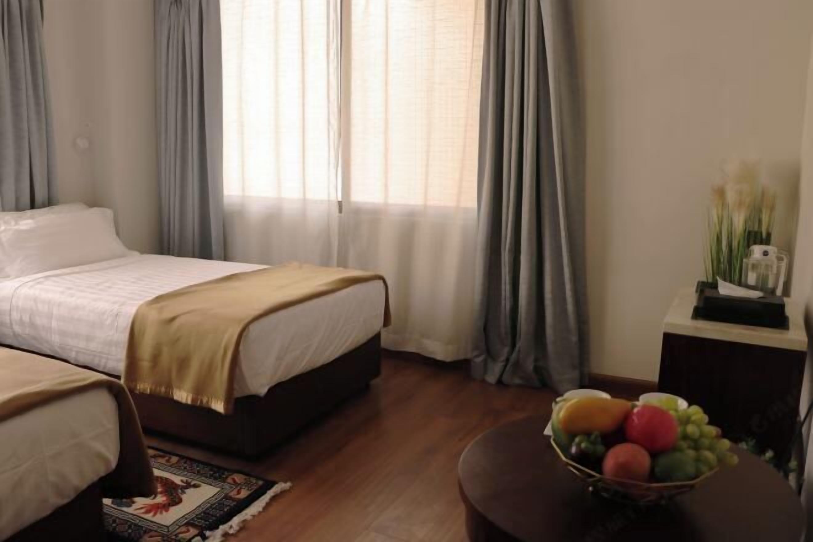 Un dormitorio con una cama, una mesita de noche con fruteros y una ventana con cortinas.