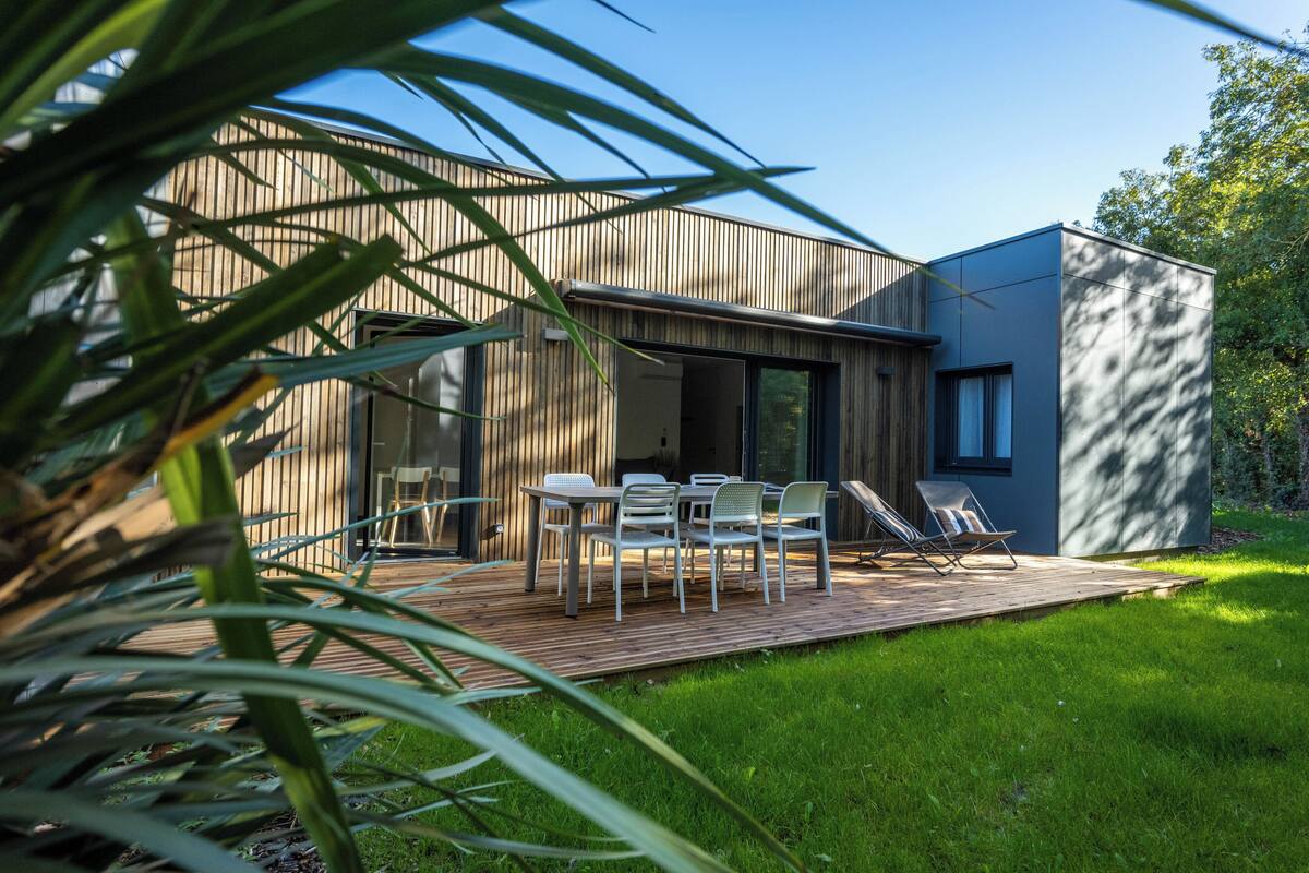 A modern house with a deck, a dining area with chairs, and a large window.