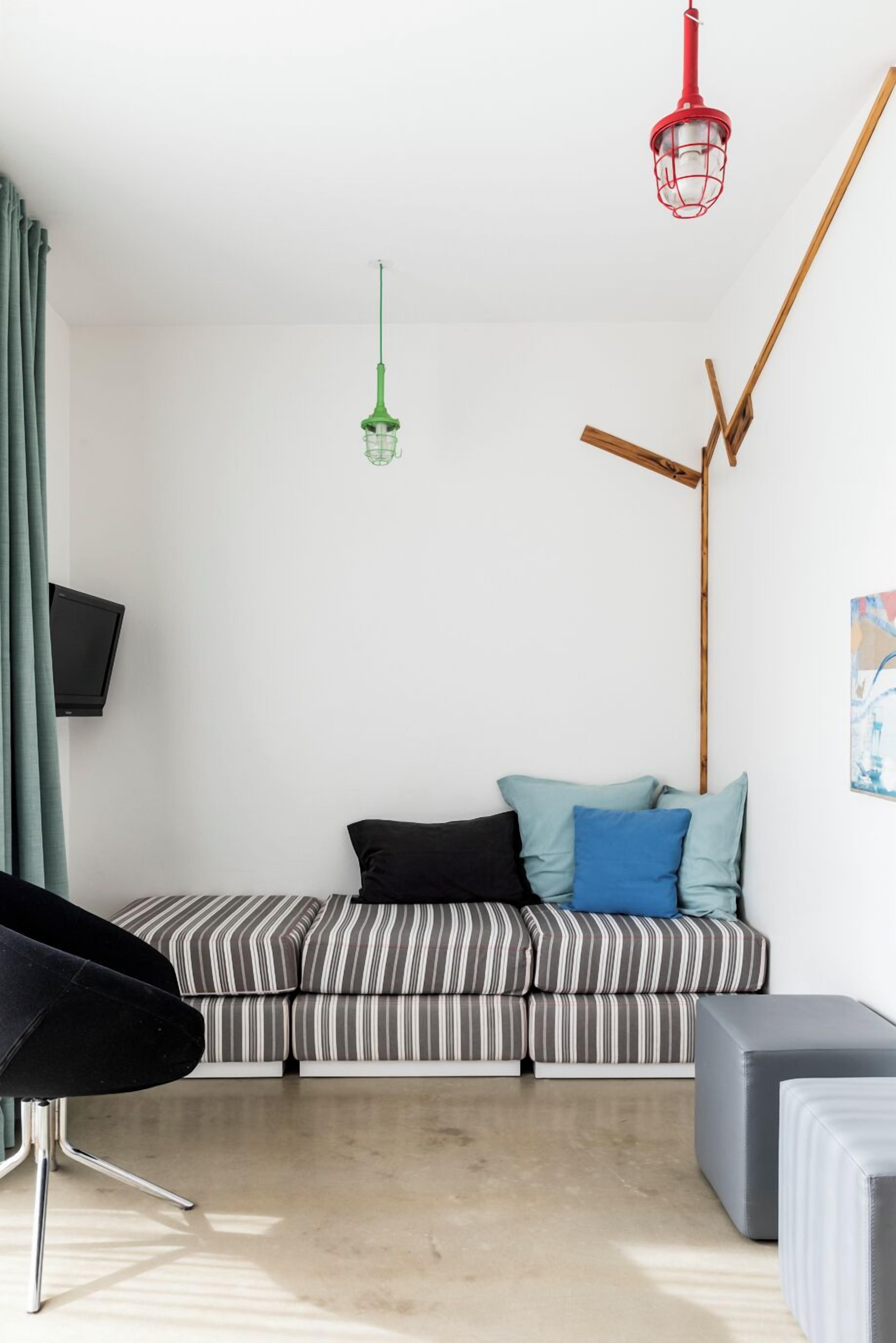 A modern living room with a striped sofa, a black chair, a grey ottoman, a television on the wall, and a red hanging light fixture.