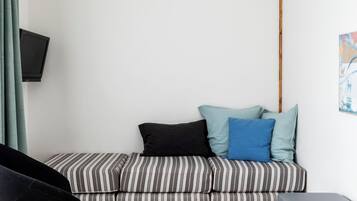 A modern living room with a striped sofa, a black chair, a grey ottoman, a television on the wall, and a red hanging light fixture.