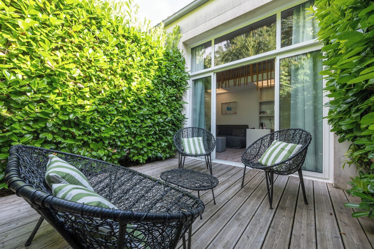 A wooden deck with wicker furniture and a green hedge.